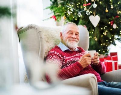 Elderly man sitting in front of Christmas tree with cup of coffee smiling