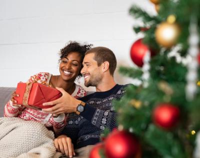 Couple sitting by Christmas tree exchanging a gift